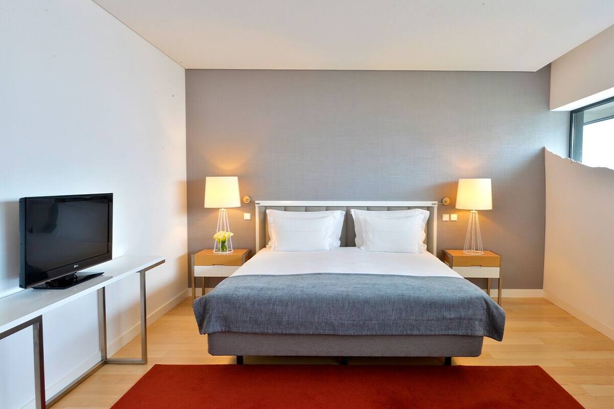 Habitación de hotel moderna con una cama, dos lámparas de noche, un televisor y una ventana.