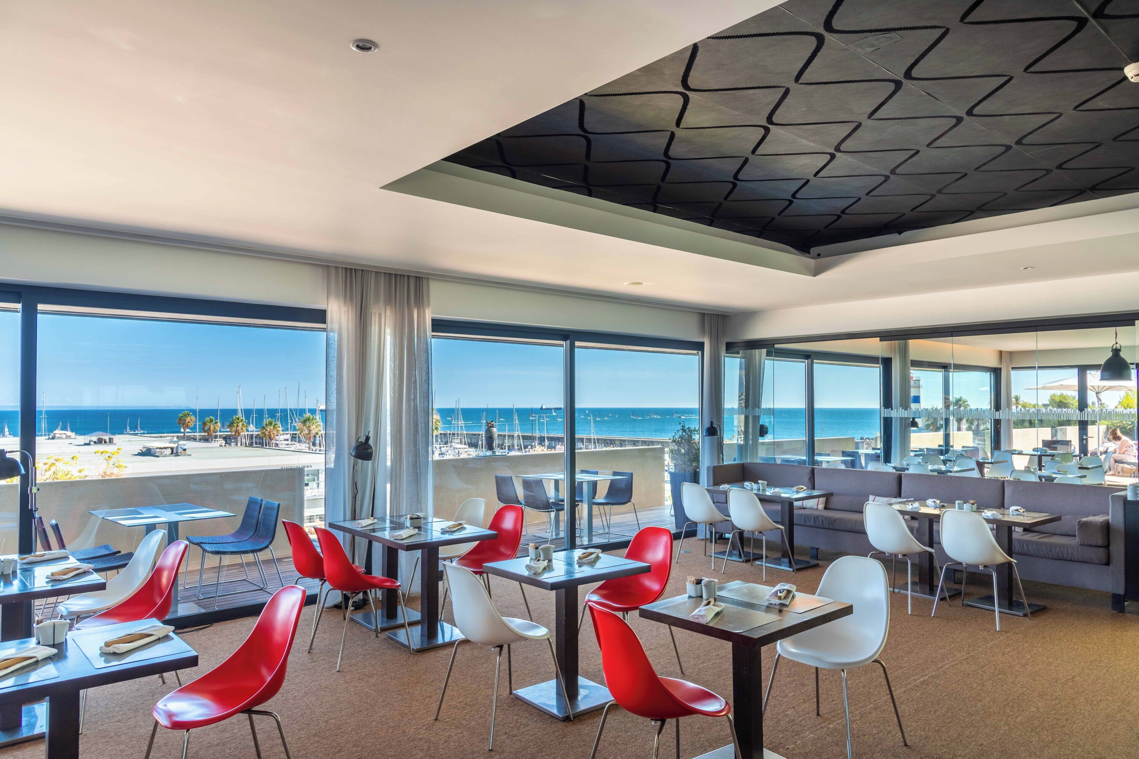 Un comedor moderno con mesas y sillas, grandes ventanales con vista a la playa y al océano.