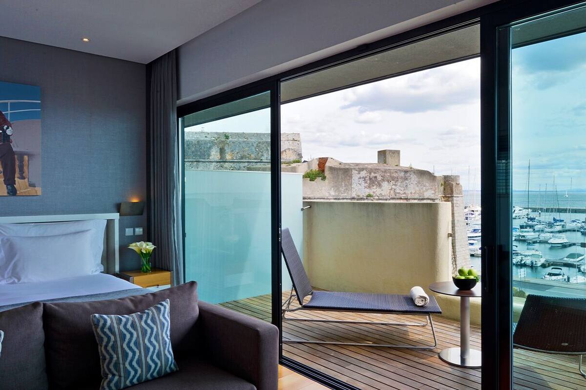 Habitación de hotel moderna con balcón, cama, sofá y vista al puerto deportivo.