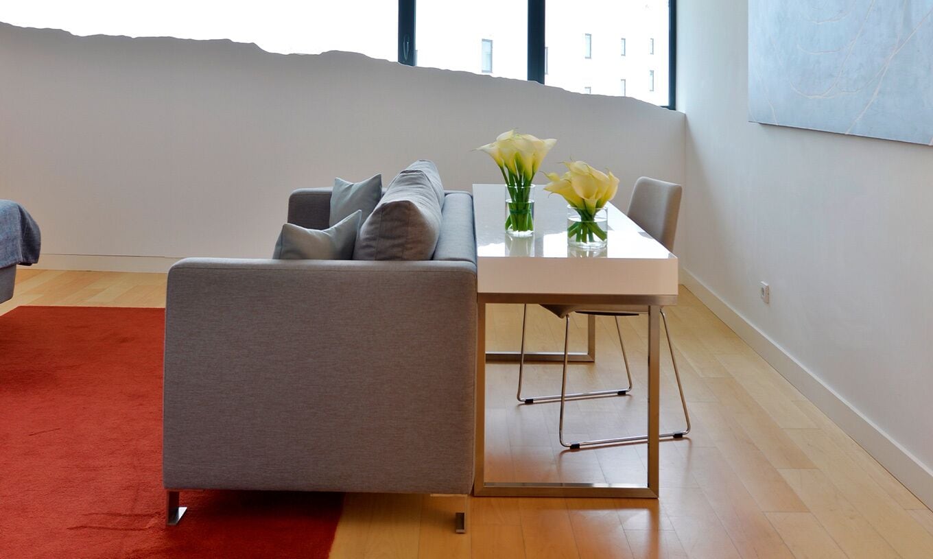 Ein modernes Wohnzimmer mit einem grauen Sofa, einem kleinen Tisch mit Blumen und einem roten Teppich.
