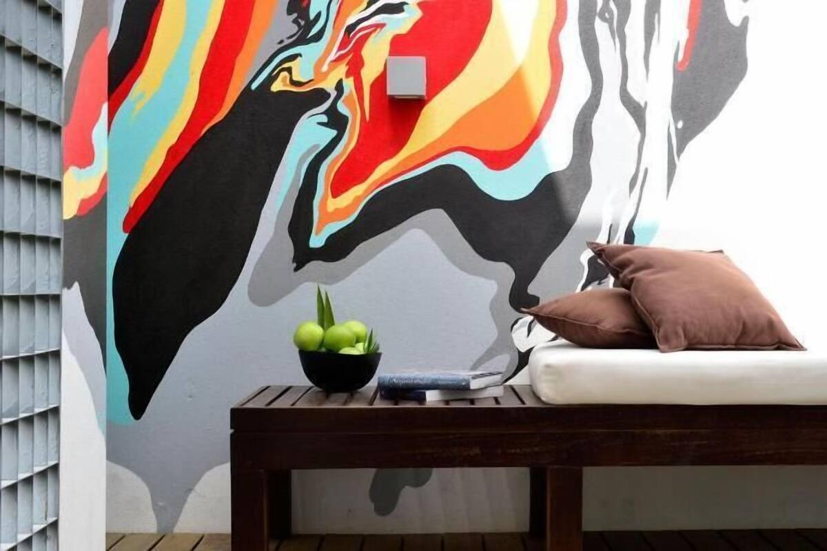 Una habitación con un mural, un banco de madera, un cuenco de fruta y un almohadón.