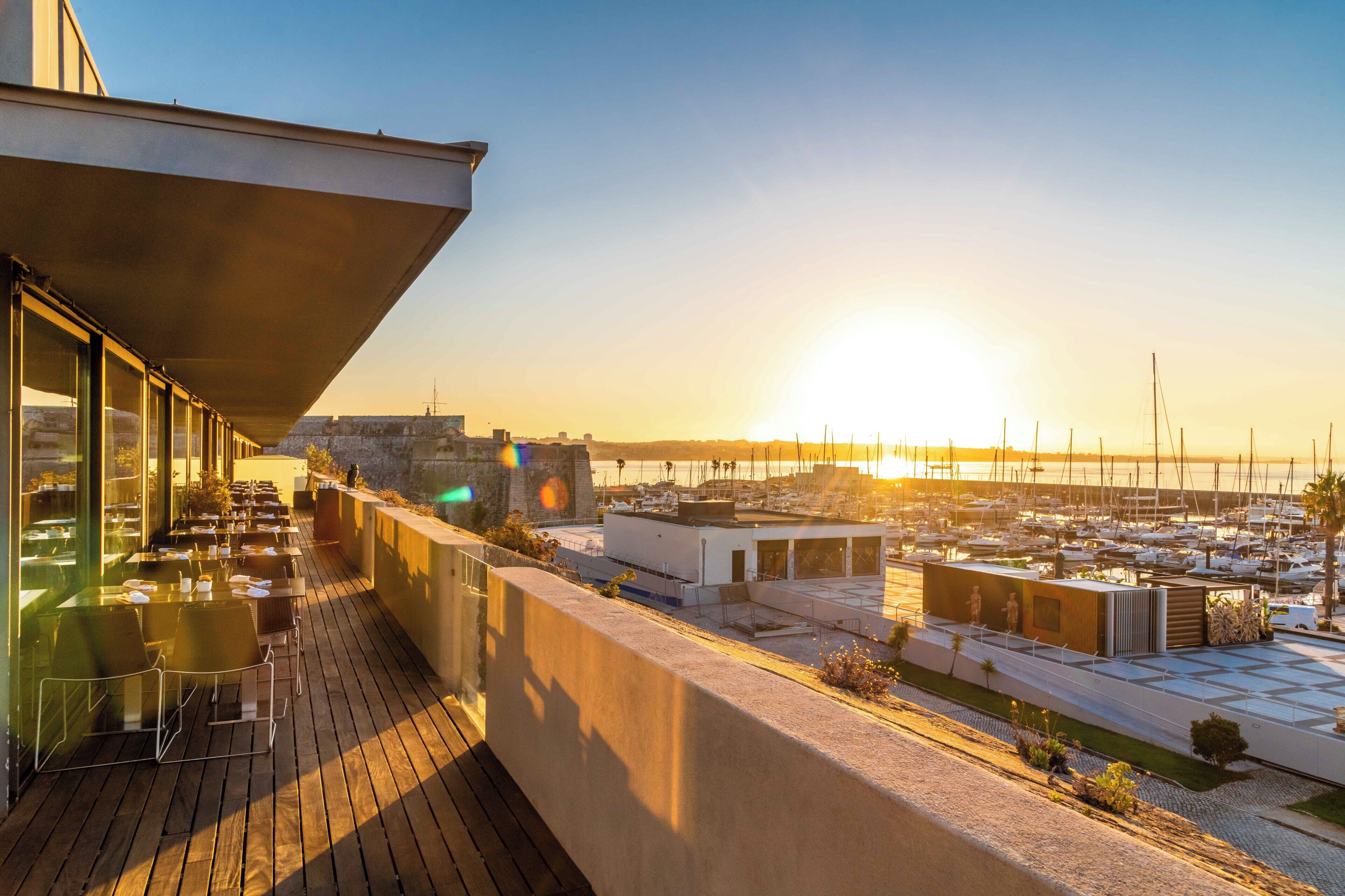 Una terrazza con posti a sedere all'aperto e vista su un porto turistico al tramonto.