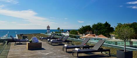 Terraza de madera con sillones de descanso y un pequeño espacio de estar, con vista a la costa y un faro a lo lejos.