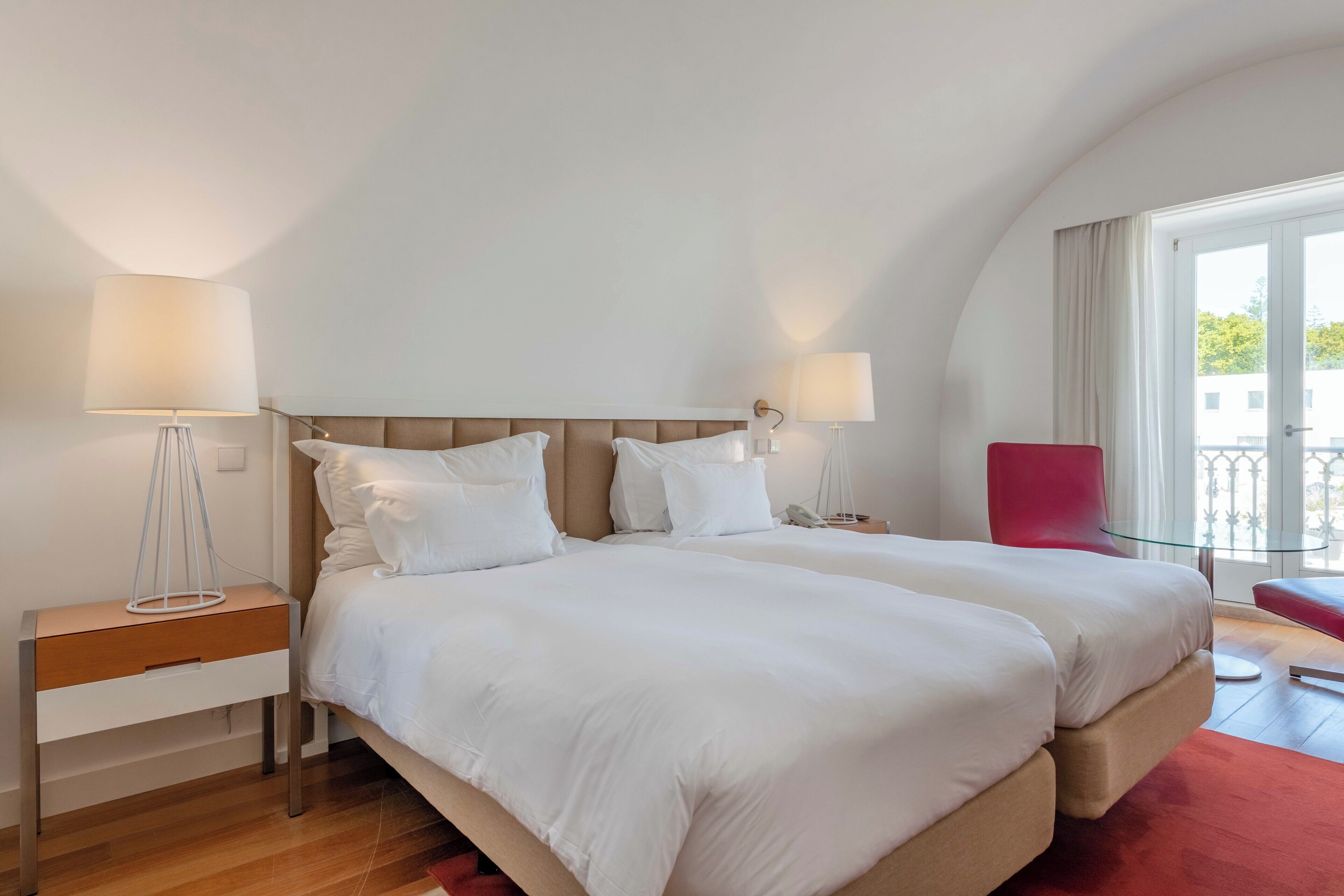 Une chambre d’hôtel avec deux lits, un fauteuil rouge et un balcon avec vue.