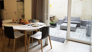 A dining area with a round table, chairs, and a glass door leading to an outdoor seating area. - Apartments Ypres (Ypres)