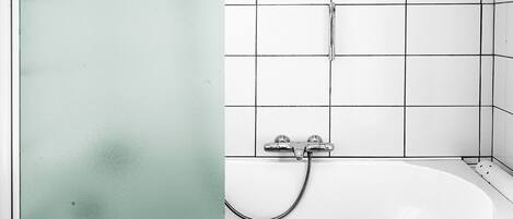 A bathroom with a white bathtub, a glass shower enclosure, and a towel rack.