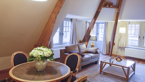 A cozy loft-style living room with a high ceiling, a round dining table with chairs, a sofa with cushions, and a coffee table with fruit. - Apartments Ypres (Ypres)