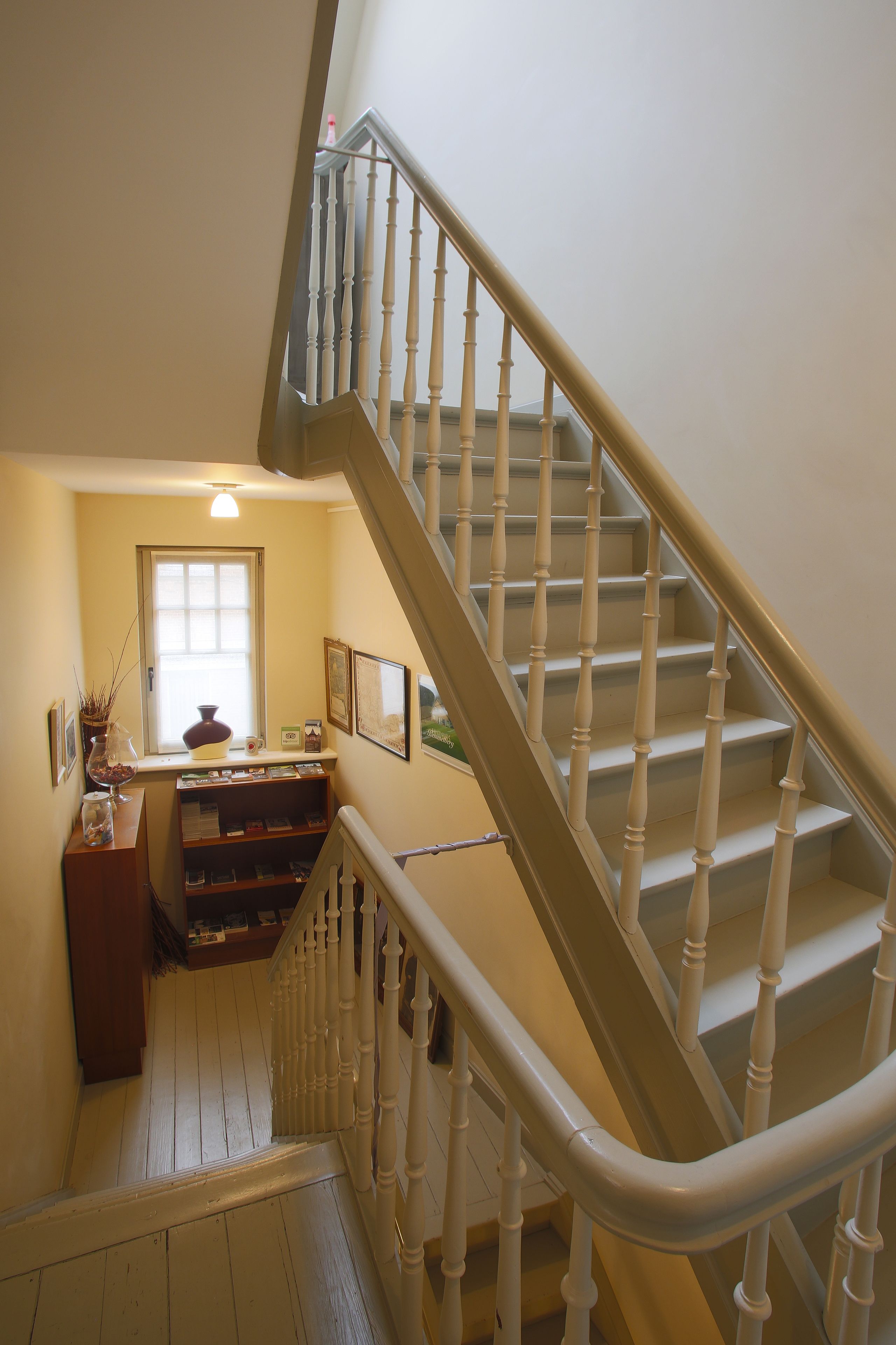 A staircase with white balusters and a wooden handrail, leading to a landing with a window and a small table with decorative items.