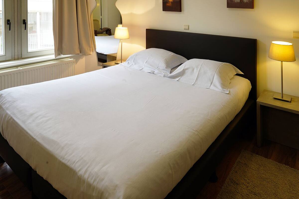 A neatly made bed with white linens in a hotel room.