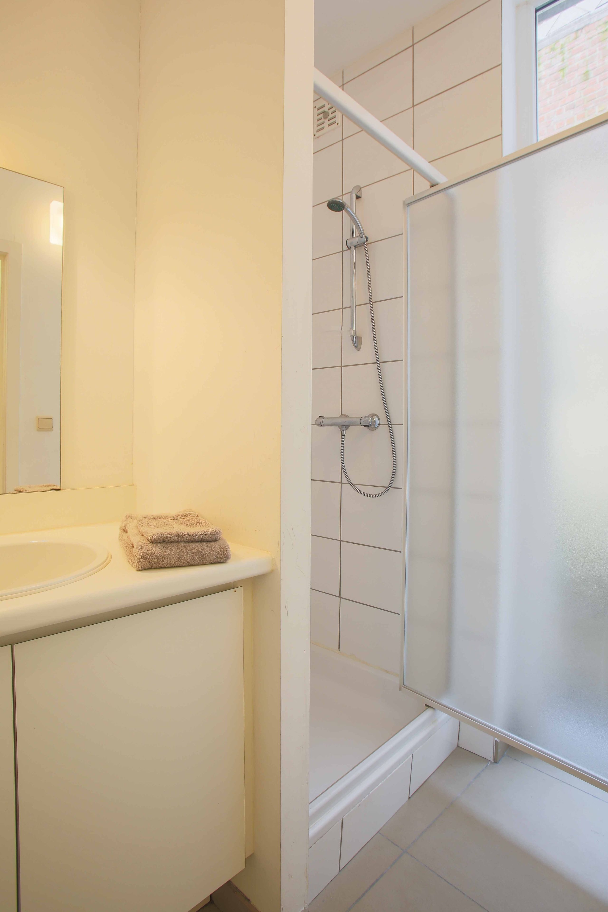 Une salle de bain équipée d’un lavabo, d’un miroir et d’une douche avec une porte en verre.