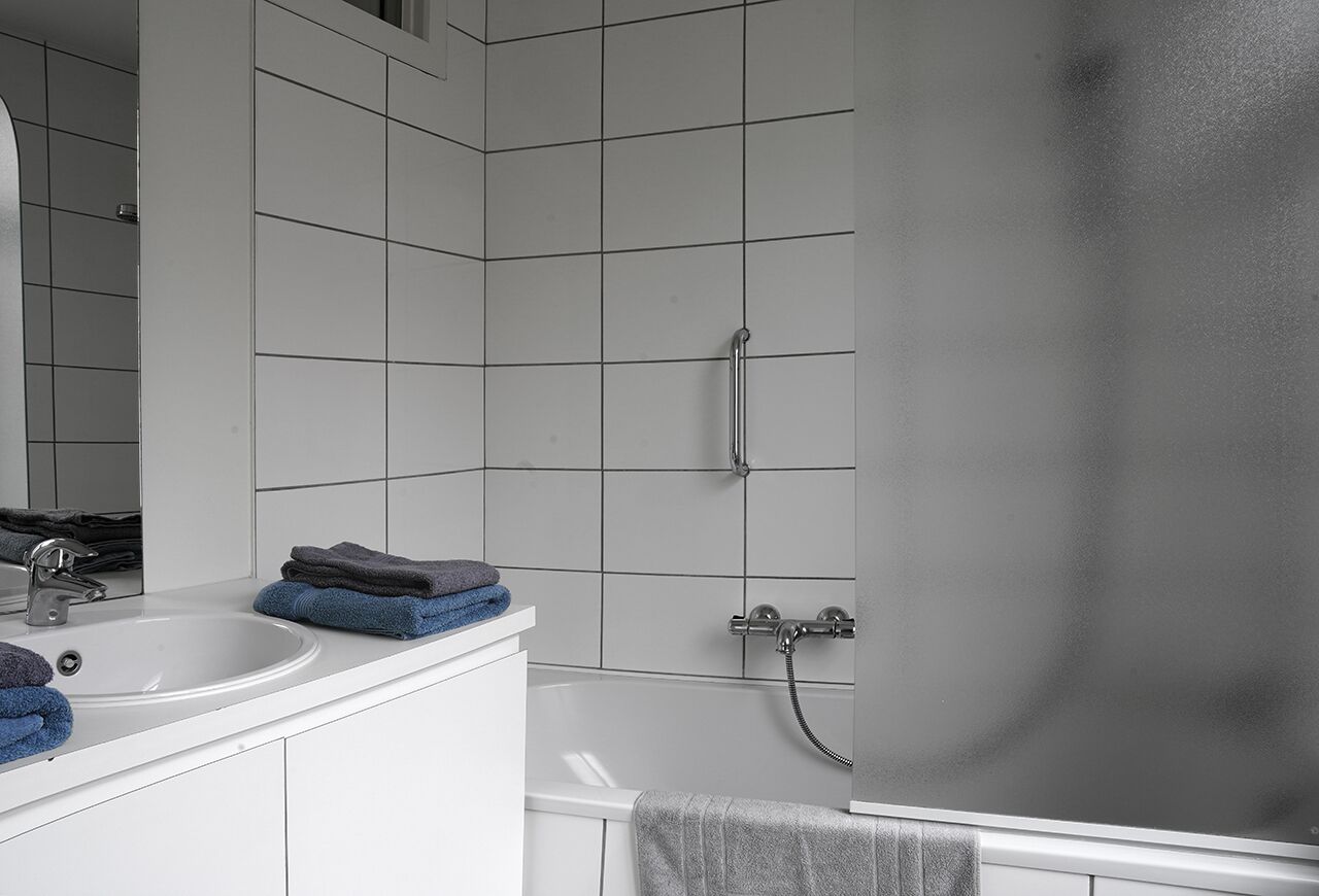 A bathroom with a white sink, mirror, and a shower with a handheld showerhead.