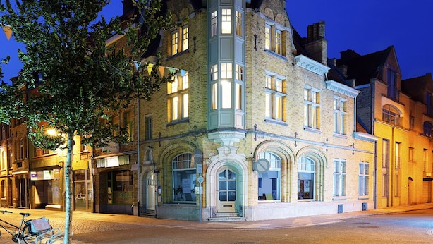 A historic building with a tower, arched windows, and a corner entrance. - Apartments Ypres (Ypres)