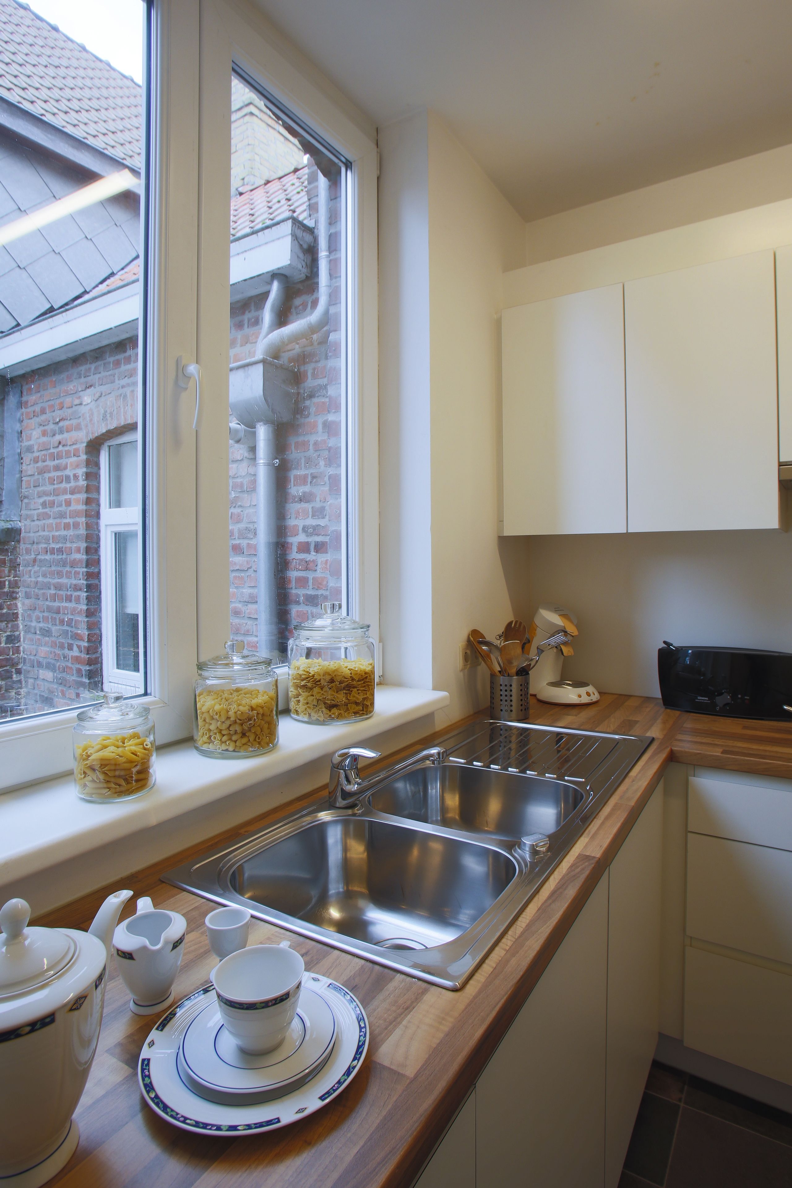 A kitchen with a window, stainless steel sink, and white cabinets.
