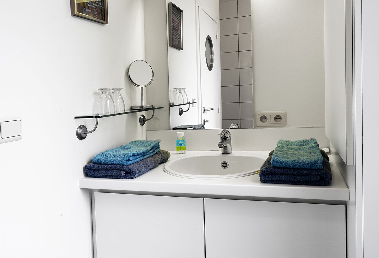 A bathroom with a white sink, two mirrors, and two towel racks with folded towels.