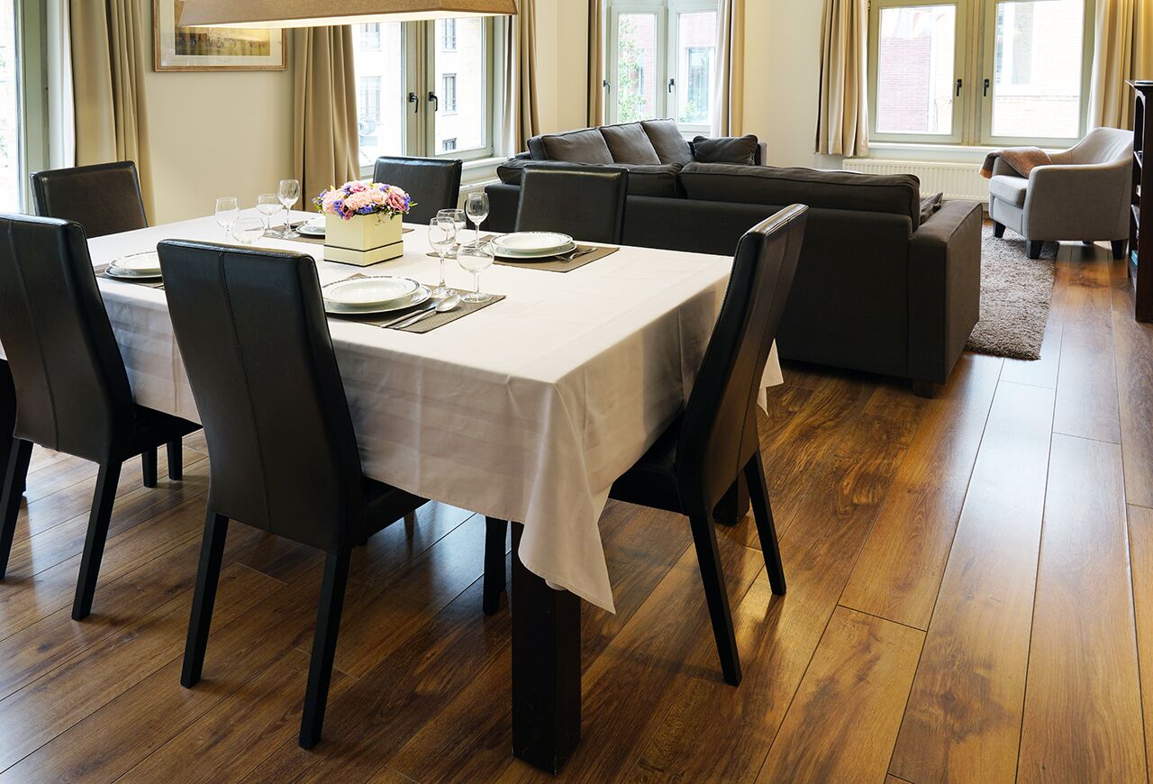 A dining area with a table set for four, a sofa, and a chair in a well-lit room with wooden flooring.