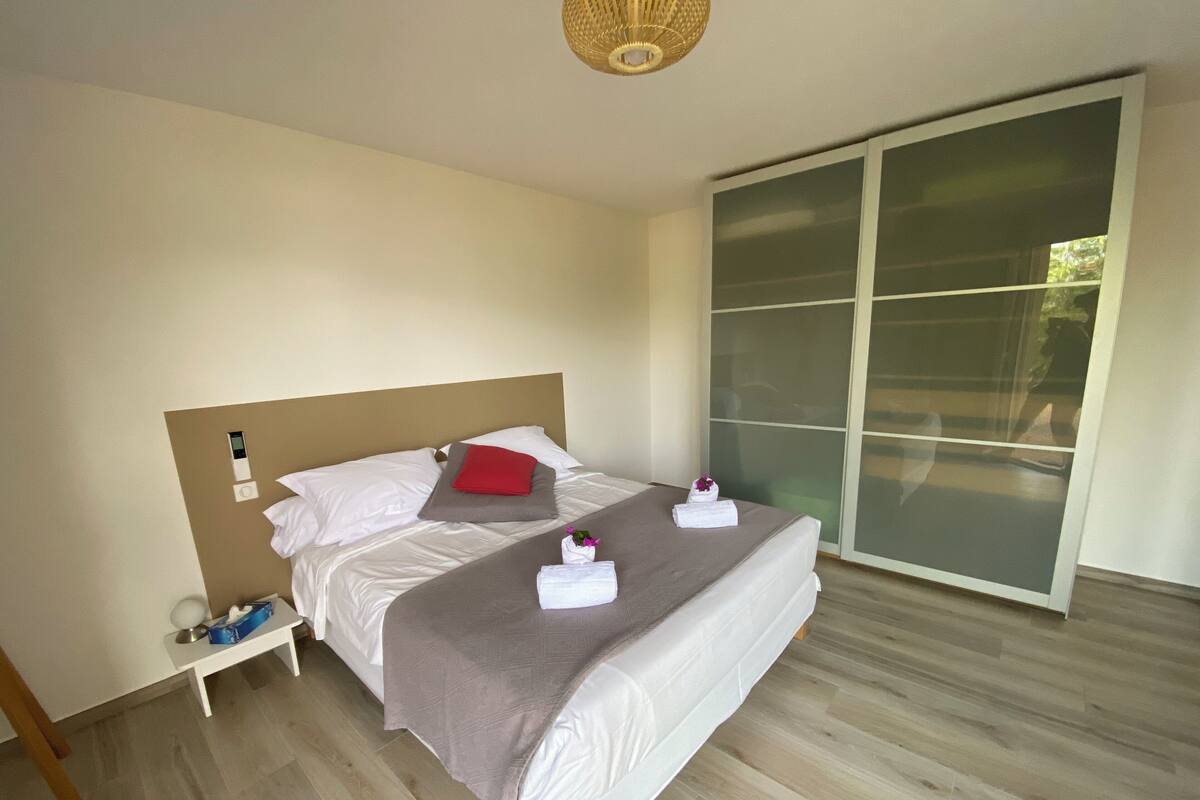 Una cama bien hecha con almohadas, una mesita de noche con una lámpara y un ventanal corredero que da a un balcón.