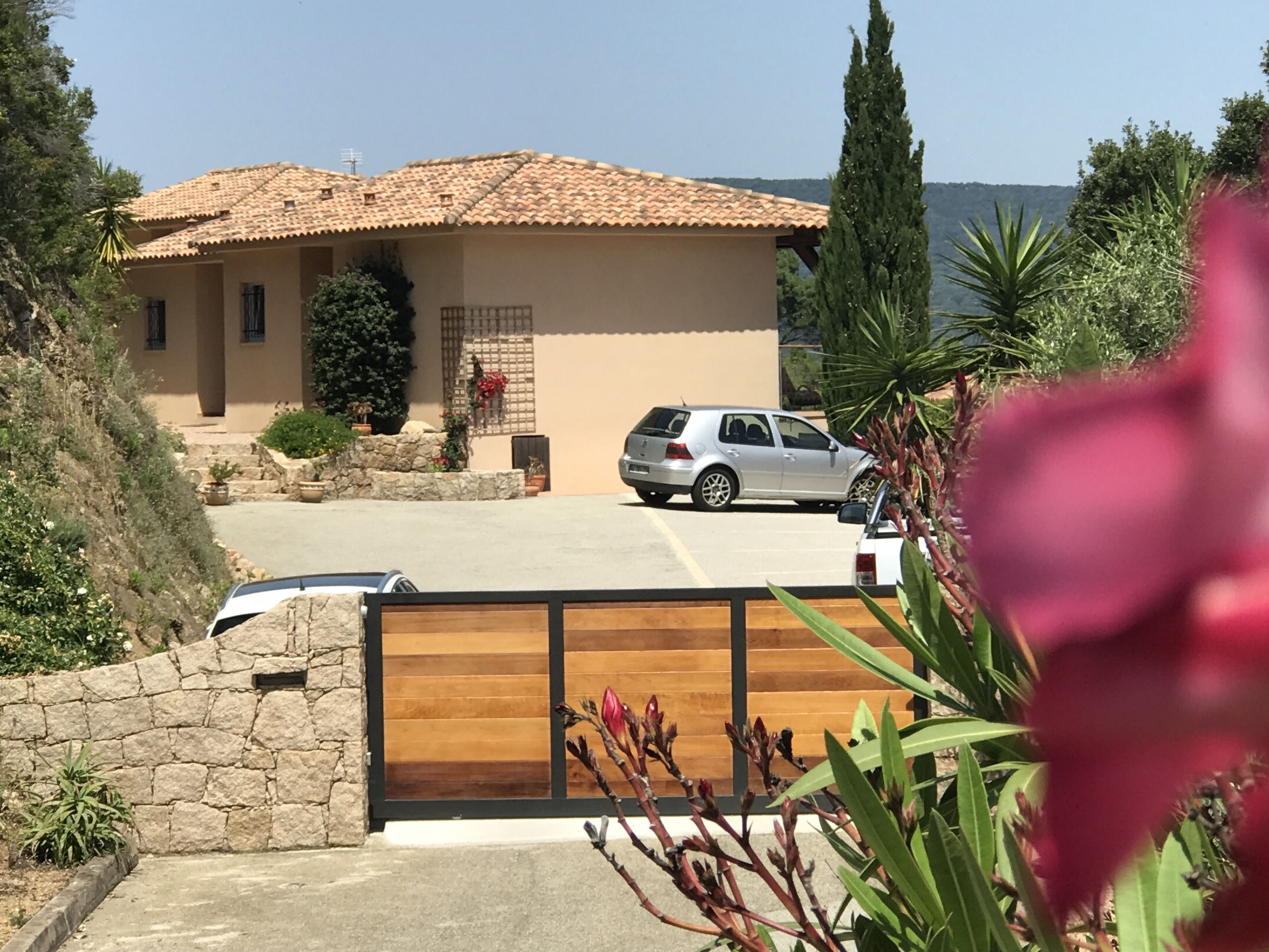A house with a tiled roof, a parked car, and a stone wall.