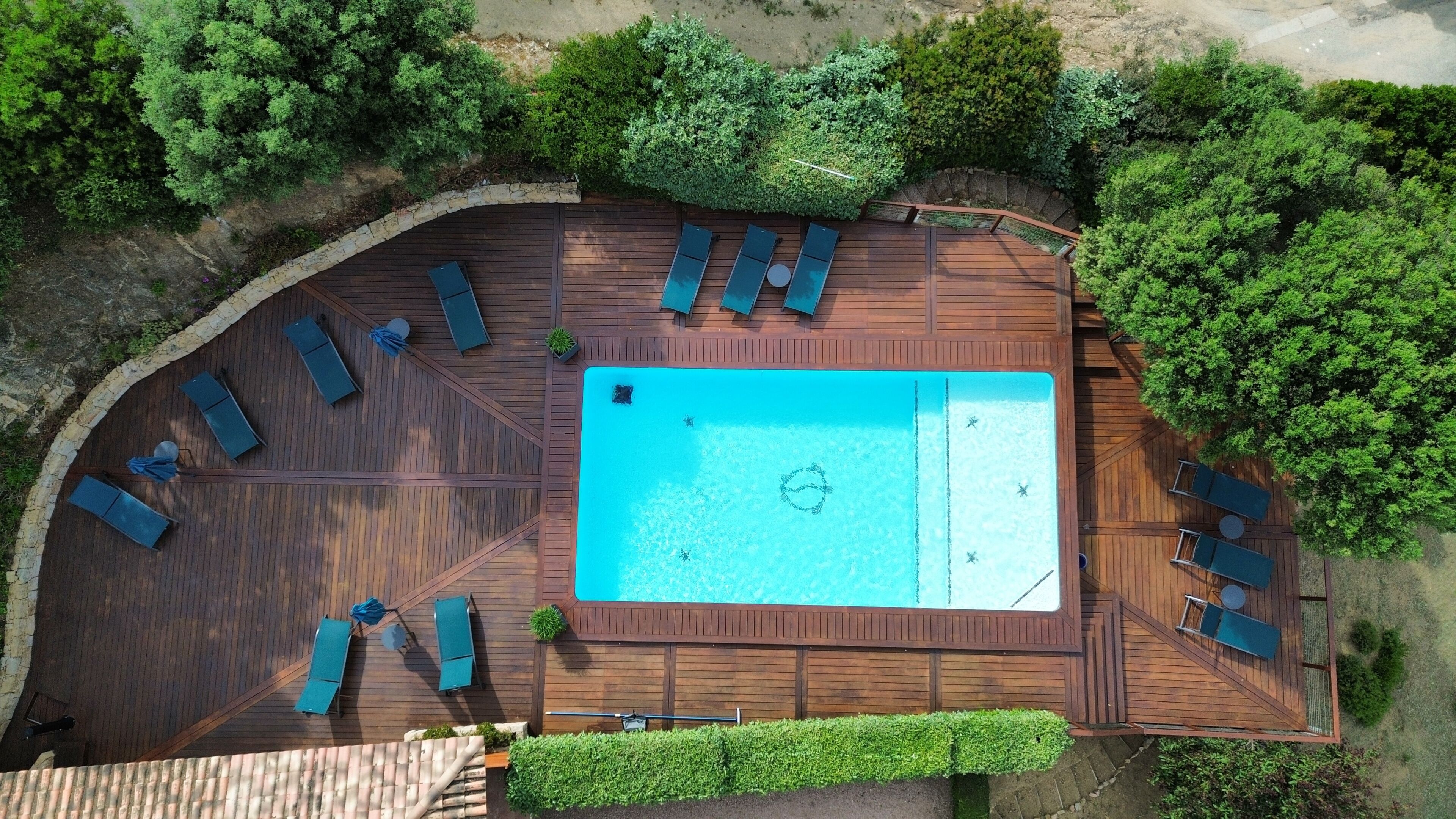 An aerial view of a wooden deck with a swimming pool, surrounded by greenery.