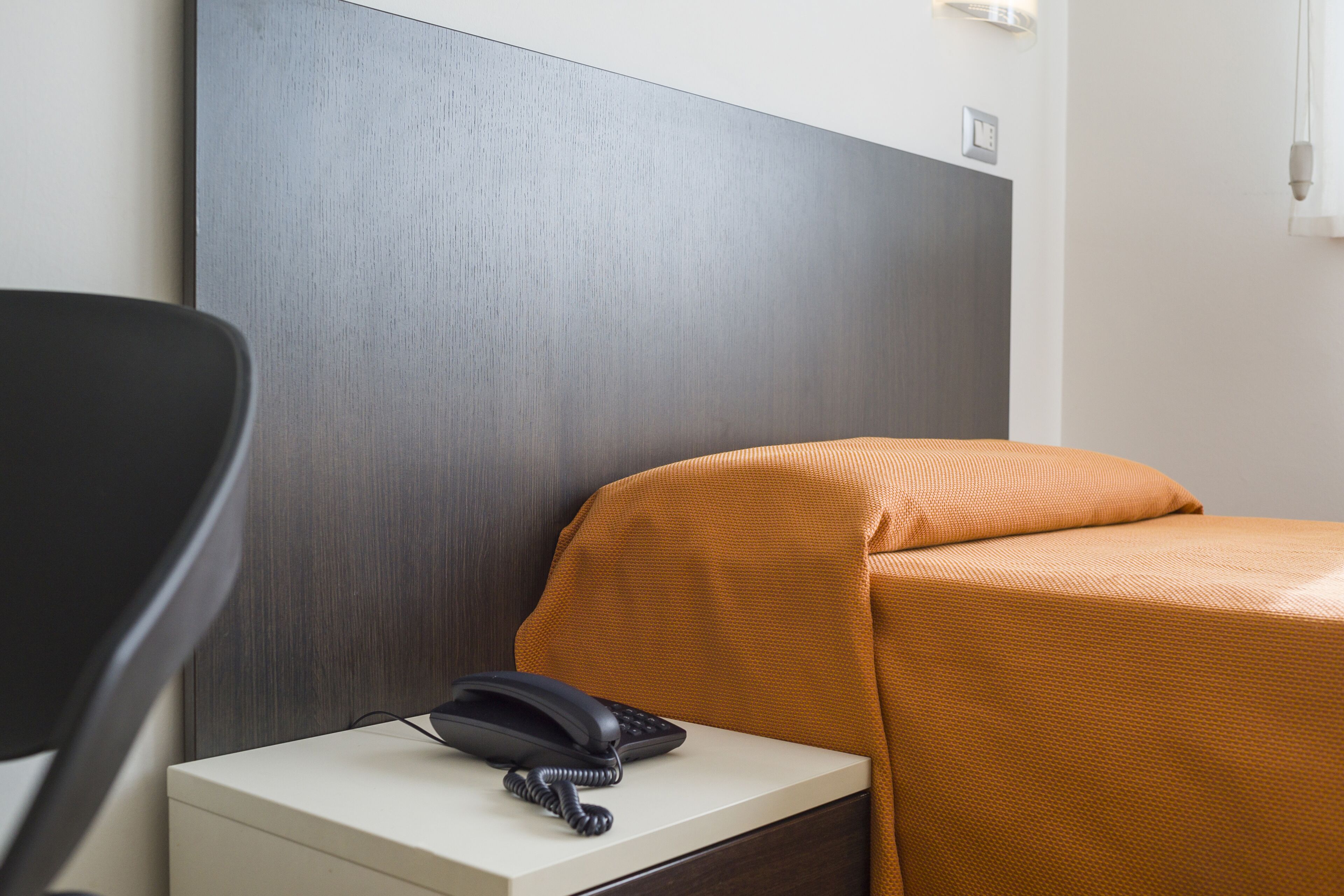 A hotel room with a bed, a nightstand, a telephone, and a chair.