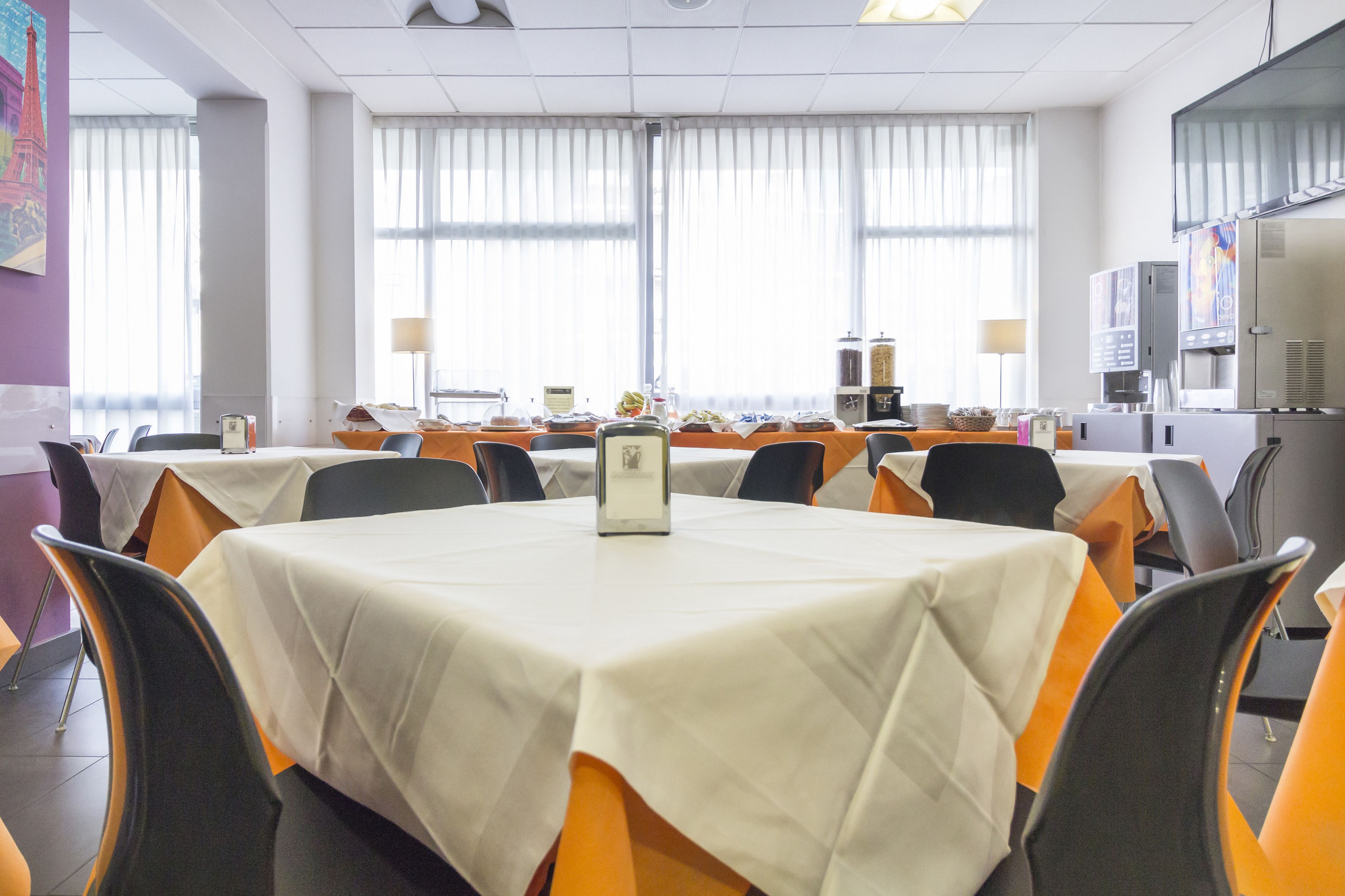 Un salón de conferencias con varias mesas, sillas y un ventanal con persianas.