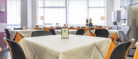 Un salón de conferencias con varias mesas, sillas y un ventanal con persianas.
