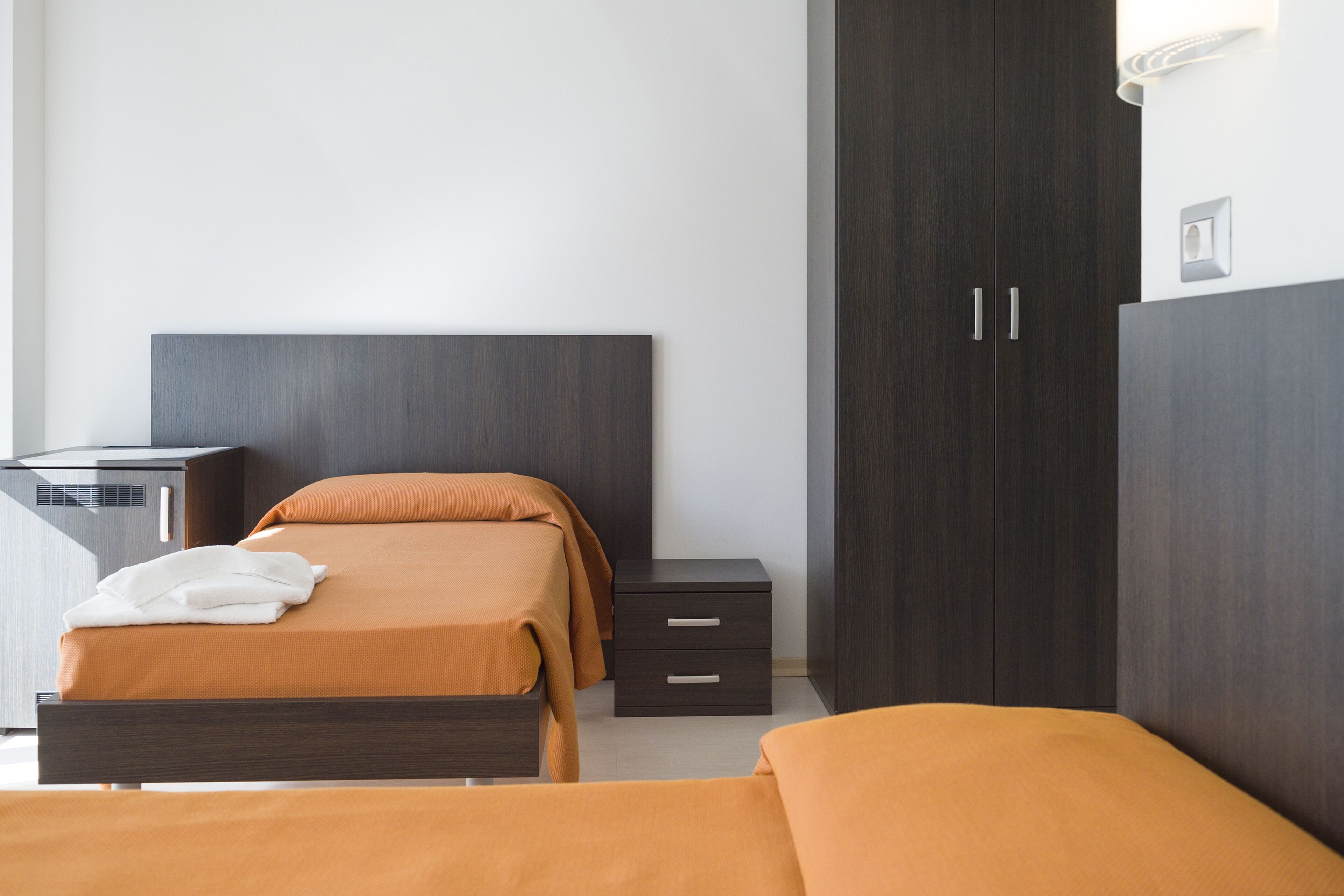 Quarto de hotel moderno com uma cama grande, mesa de cabeceira, guarda-roupa e escrivaninha com cadeira.