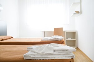 Una camera d'albergo con due letti, una finestra e uno scaffale con asciugamani.