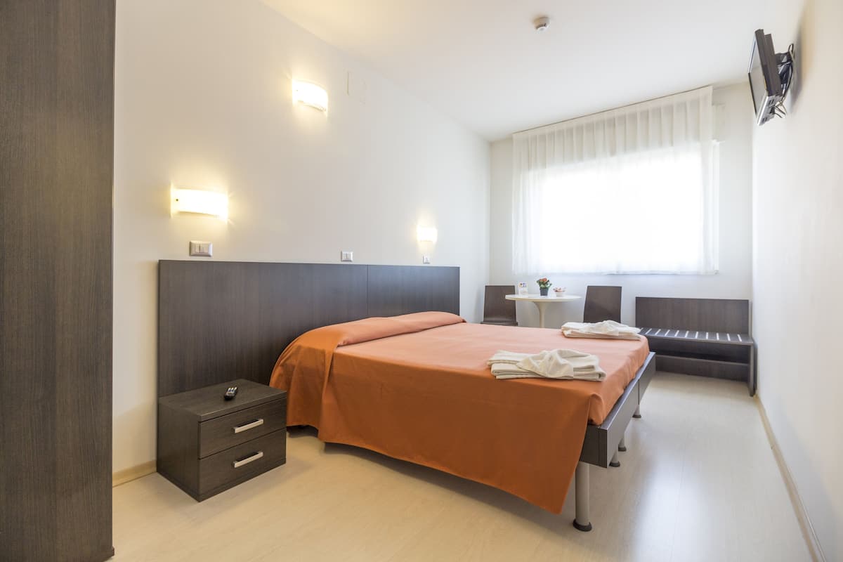 Hotellihuone, jossa on sänky, yöpöytä ja pieni työpöytä tuolilla.