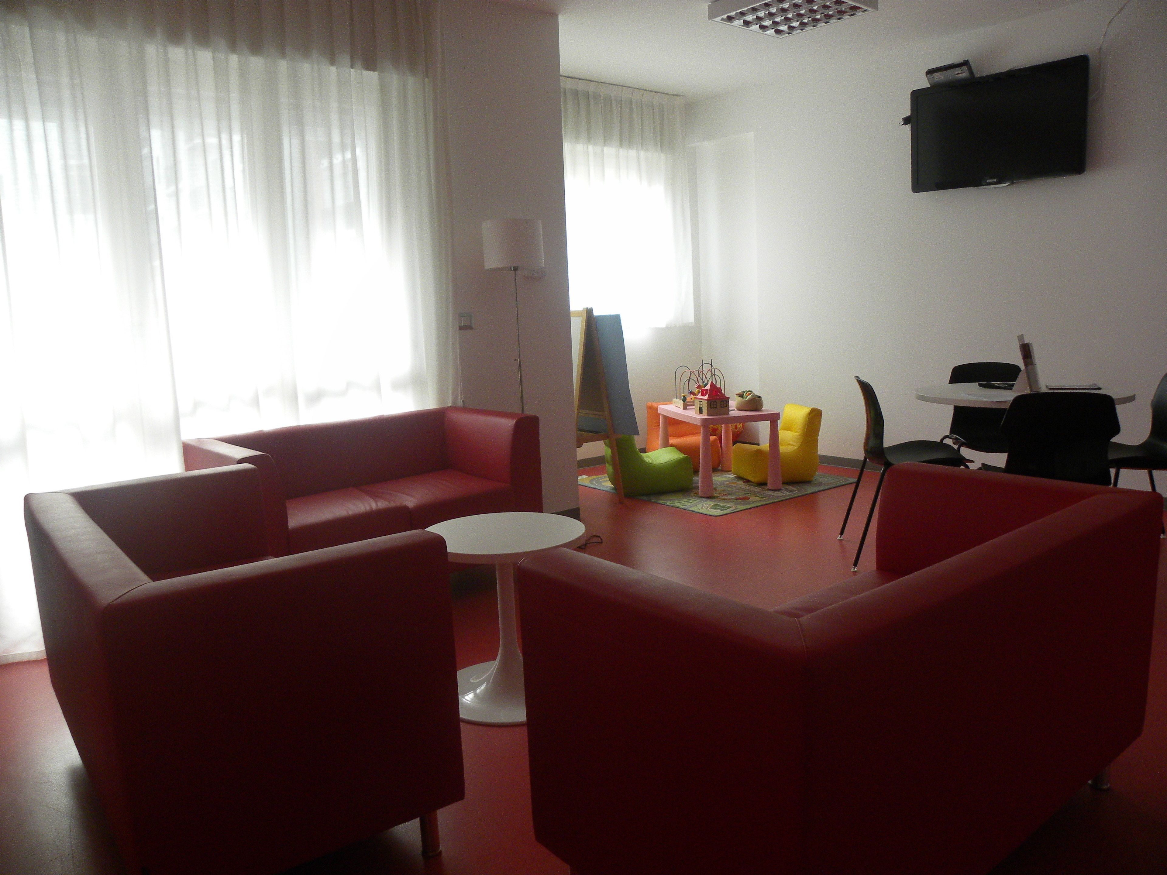 A living room with red sofas, a small white table, and colorful chairs.