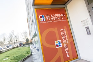 A building entrance with a sign for 'SHARING TORINO' indicating it offers housing sociale, residence, and hotel services.