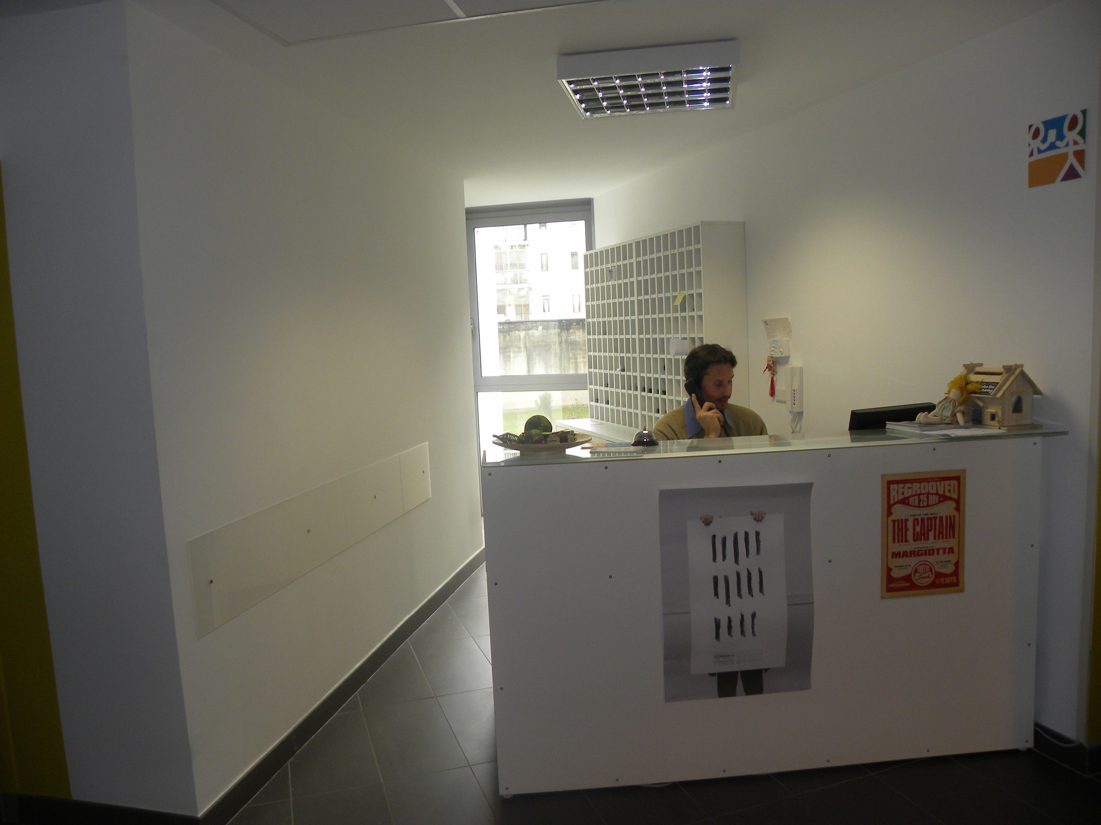 Ein Empfangsschalter mit Fenster, ein kleines Hausmodell und ein Poster an der Wand.