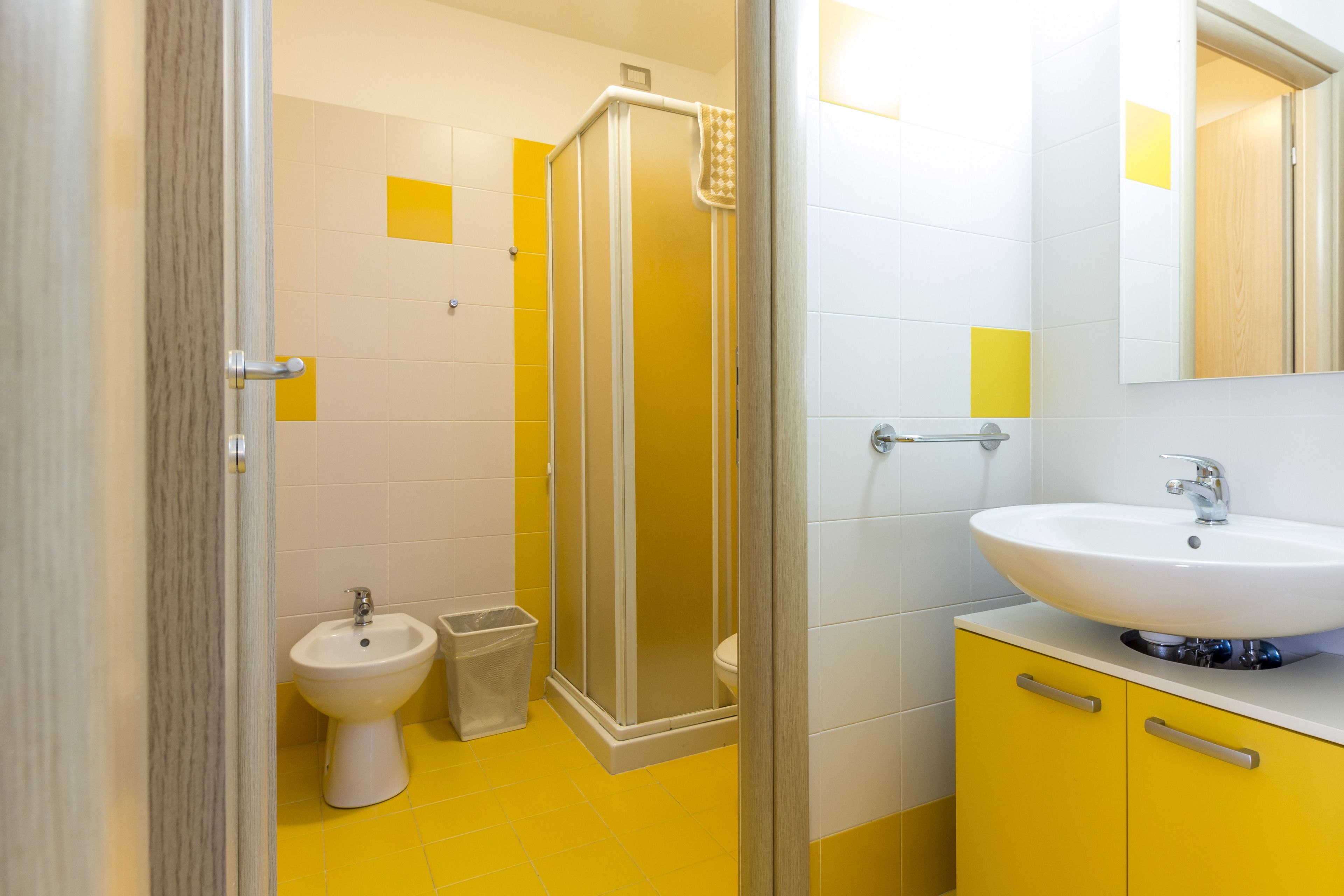 A bathroom with a yellow floor, a white sink, a bidet, and a glass shower enclosure.