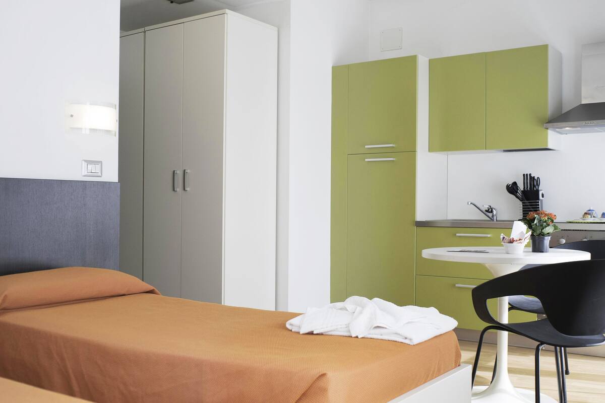 Hotellihuone, jossa on sänky, työpöytä ja vihreät kaapit.
