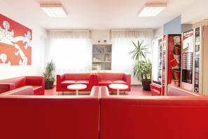 A modern living room with red sofas, a coffee table, and a bookshelf. There is a vending machine and a plant in the room.
