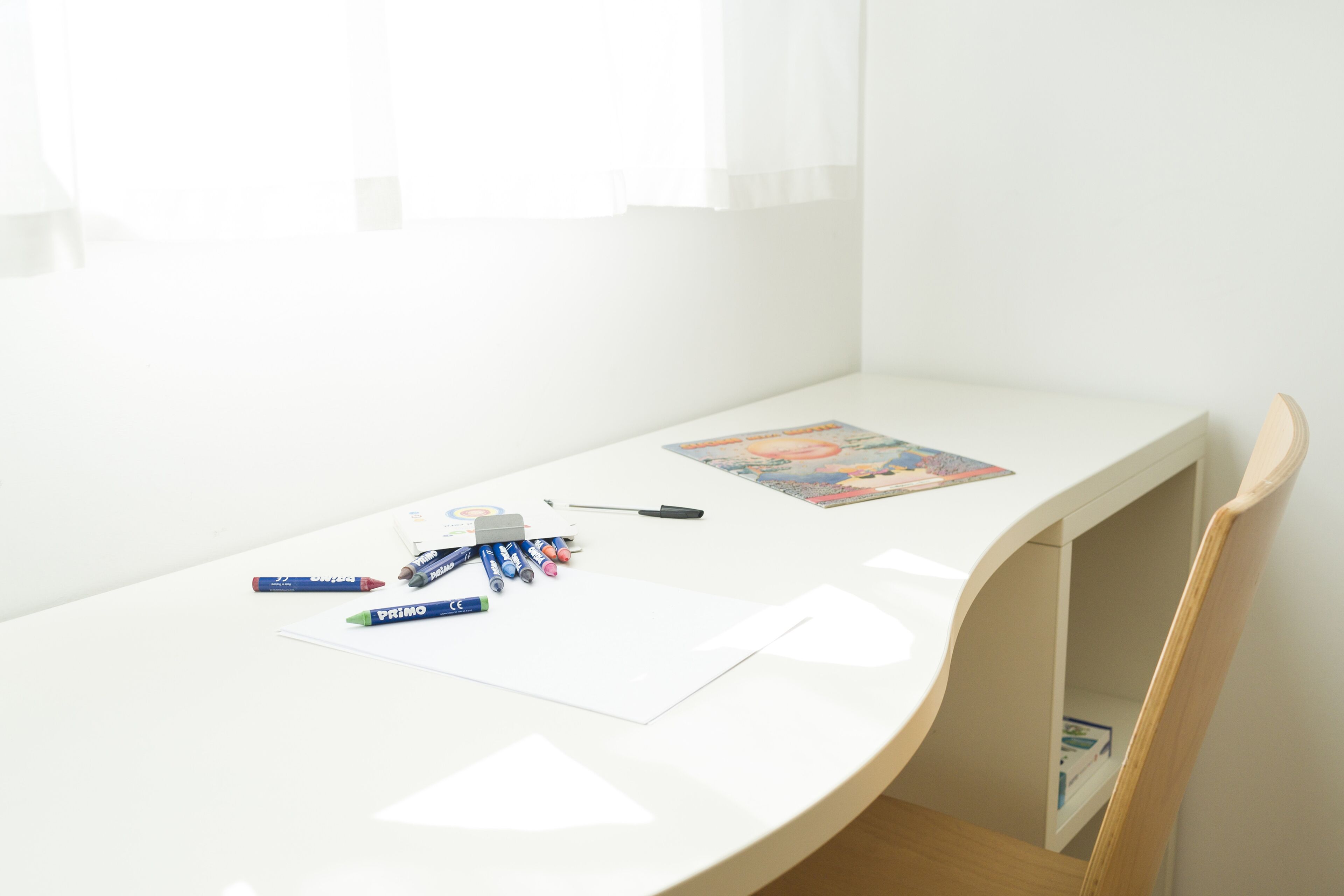 Un escritorio blanco con un libro, marcadores y una pluma.