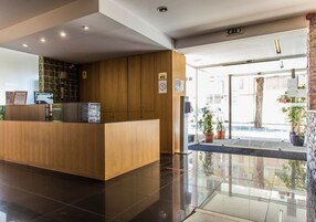 A reception desk with a wooden finish, a glass door entrance, and potted plants outside.