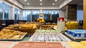 A buffet with various food items and beverages, arranged on tables with a view of the outdoors through large windows. - Hotel Columbano (Peso da Régua)