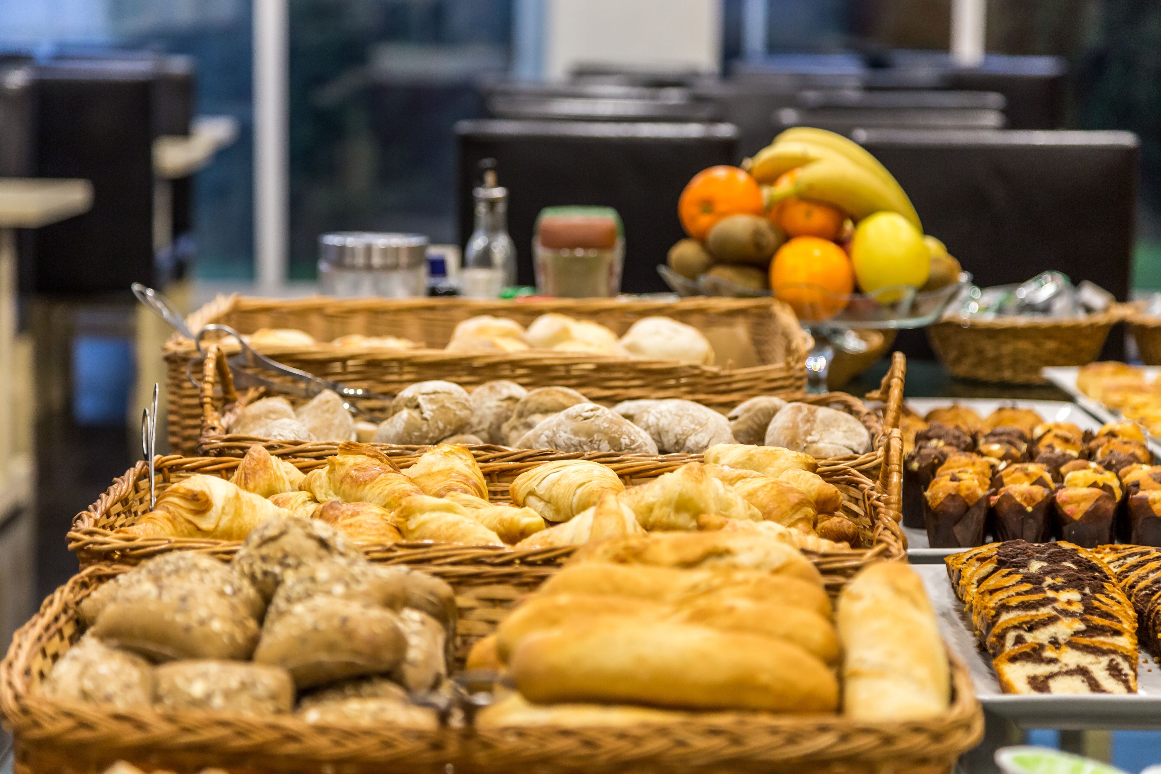 A buffet with various breads, pastries, and fruits.