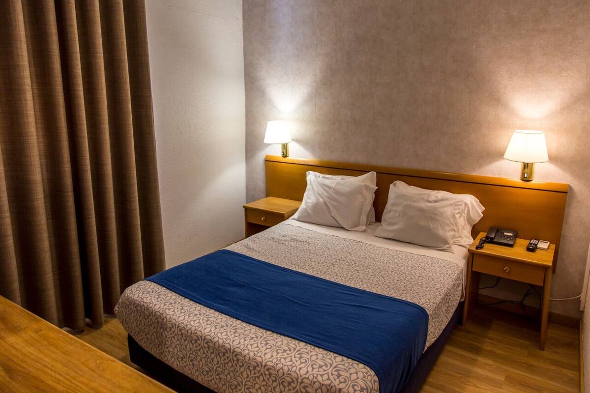 A hotel room with a bed, two bedside tables, a lamp on each table, and a curtain on the window.