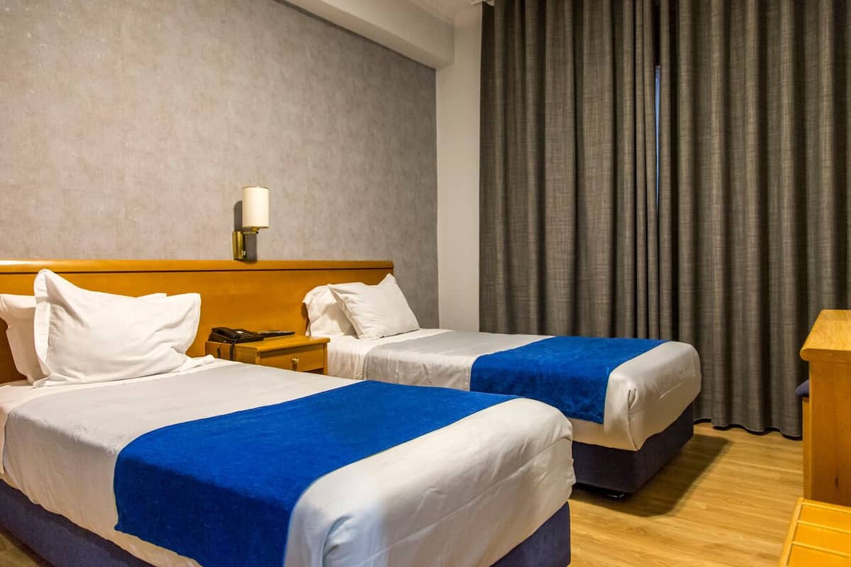 A hotel room with two beds, a nightstand, a lamp, and a wooden desk.