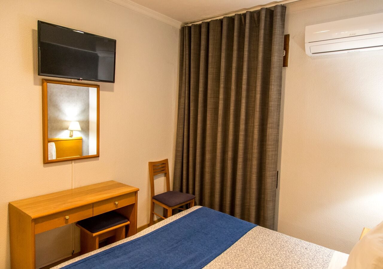 Habitación de hotel con cama, escritorio, silla, televisor montado en la pared y aire acondicionado.
