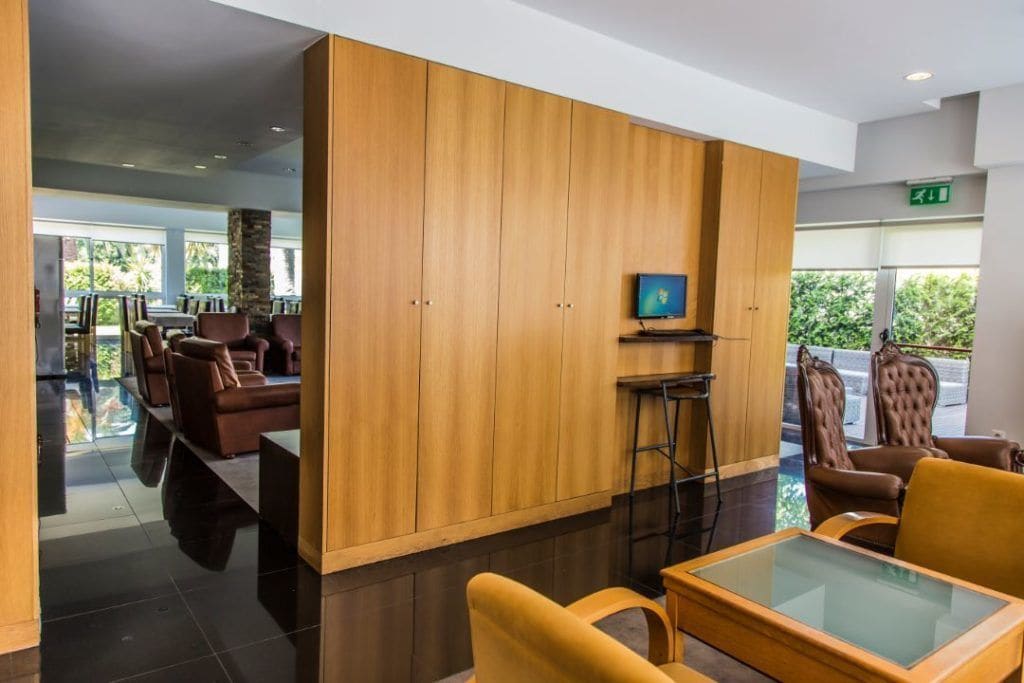 A modern lobby with a wooden partition, comfortable seating, a television, and a glass table.