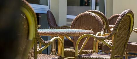 Wicker furniture with a glass table and chairs, positioned outdoors with a building in the background.