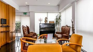 A modern hotel lobby with leather chairs, a piano, and a glass table with a laptop.