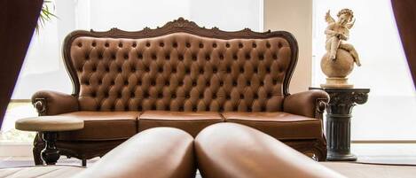A brown leather sofa with a tufted backrest, positioned in a room with a statue of a cherub on a pedestal.