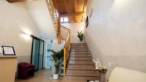 A staircase with wooden railings leading to an upper floor, a reception desk with a chair, and a potted plant. - Hotel Residence Sestriere (Moncalieri)