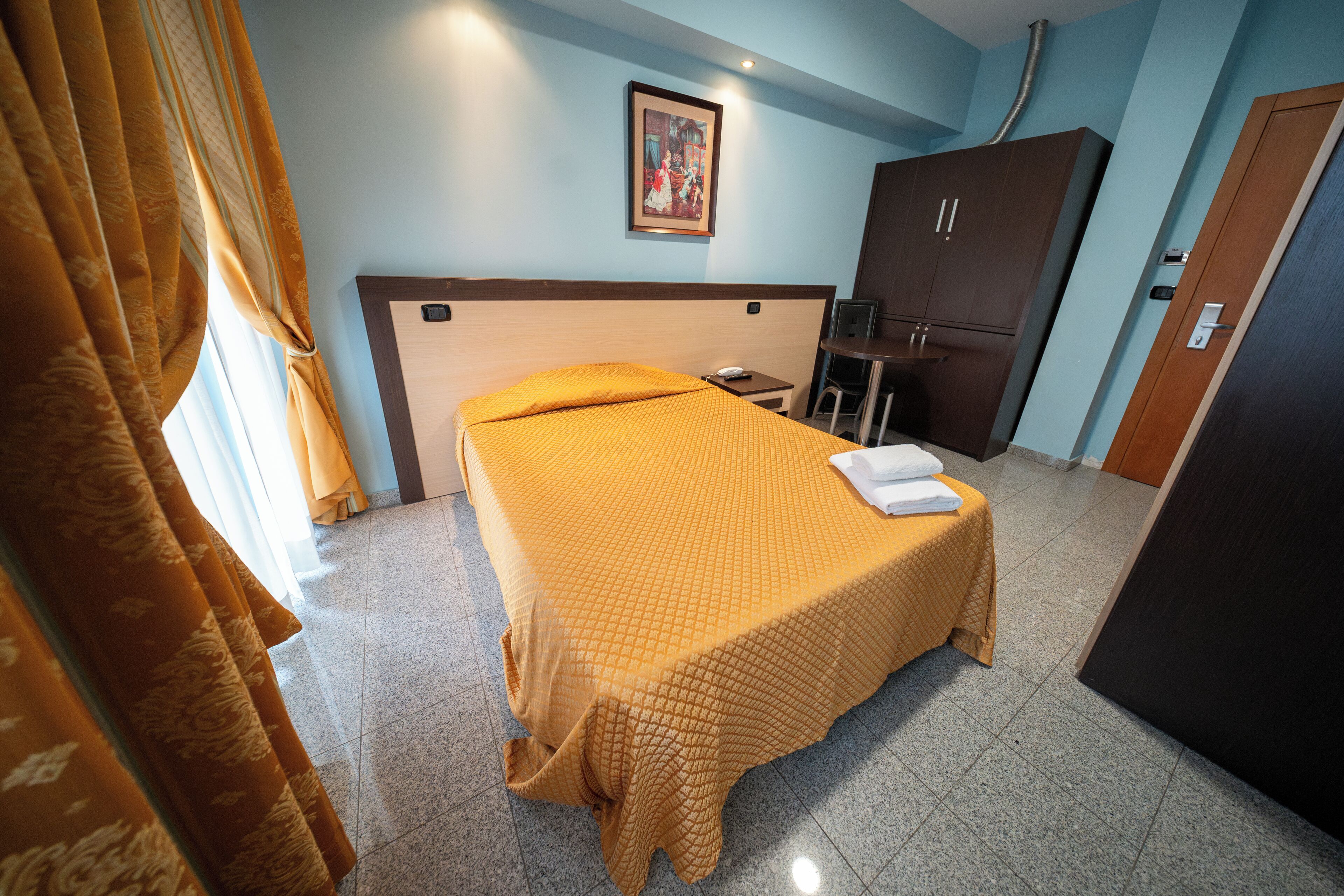 A hotel room with a bed, a desk, a chair, and a wardrobe.