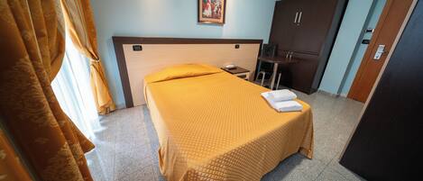 A hotel room with a bed, a desk, a chair, and a wardrobe.