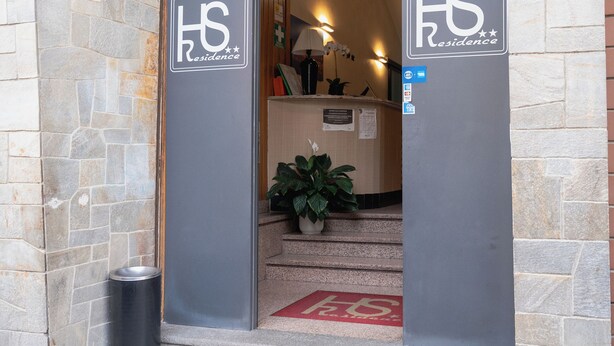 A hotel entrance with a stone facade, wooden paneling above the door, and a sign indicating the name 'HS Residence'. - Hotel Residence Sestriere (Moncalieri)