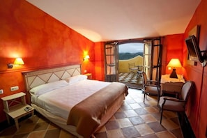 A hotel room with a bed, bedside table, lamp, and a view of the outdoors.